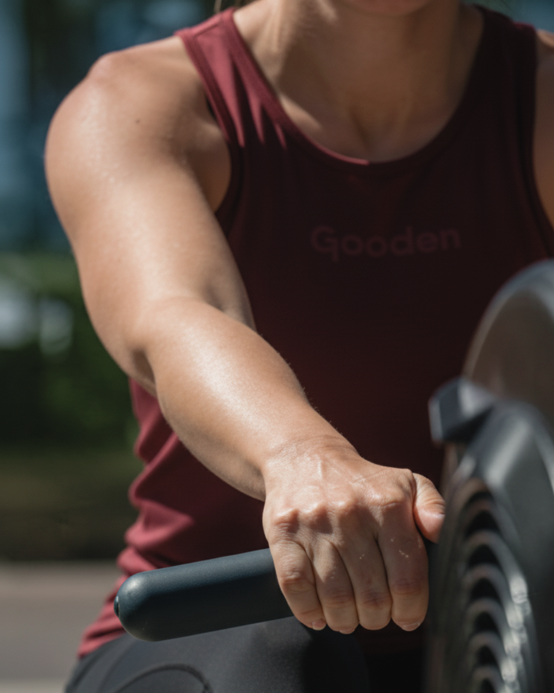 Frau trainiert am Rudergerät und trägt rotes Sport Tanktop von GOODEN Sportswear – nachhaltige Sportswear Damen, atmungsaktiv und funktional fürs Gym