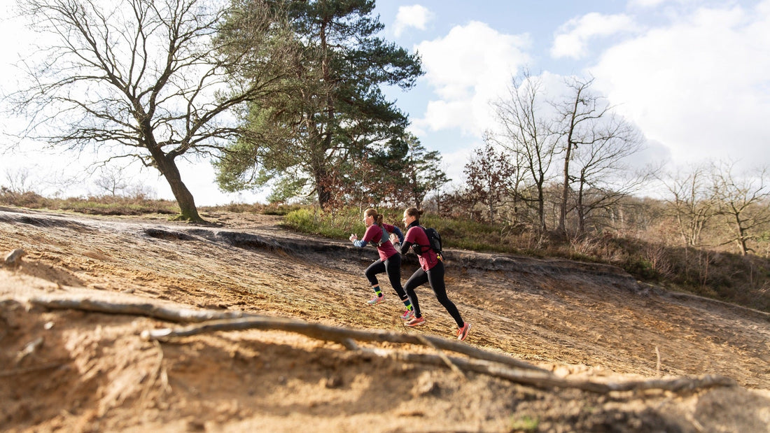 Two women running up a hill in the forest and show that the fabric of GOODEN Sportswear is very durable. 