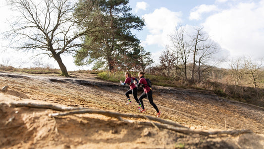 Two women running up a hill in the forest and show that the fabric of GOODEN Sportswear is very durable. 